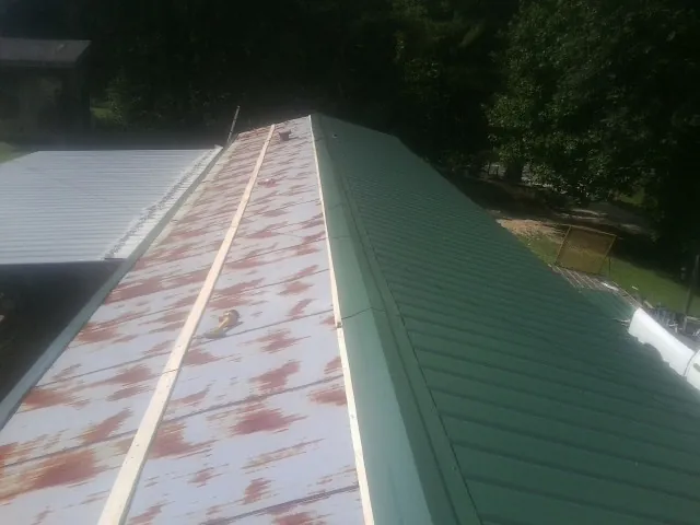 Old rusted panels beside newly installed green metal roofing — Wind Damage Roof Repair by Roofing Brothers in Spring Valley